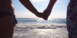 年轻的情侣站在海边，欣赏美丽的风景。在海滩上，男性和女性的手臂互相爱抚。暑假或假期。近点后视图