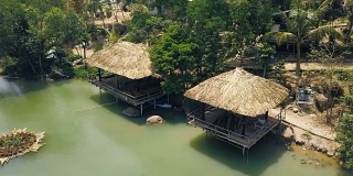 夏日茅草屋顶的小屋在岸边的山湖与绿色的水在热带自然之间休息。夏季凉亭在湖滨无人机视图