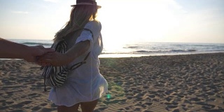 跟着我拍的年轻女子穿着衬衫背着背包拉着男友去海边。幸福的夫妇花时间一起在户外。暑假或假期概念。慢镜头观点
