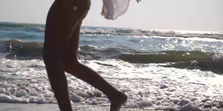 女性的脚在潮湿的沙子和海浪在海滩的海水上奔跑的特写。年轻女子在岸边奔跑的双腿。光着脚的女孩在海边。暑假或假日概念。慢动作侧视图低角度视图
