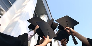 快乐的学生们穿着长袍，把学位帽抛向空中。教育、毕业与人理念-