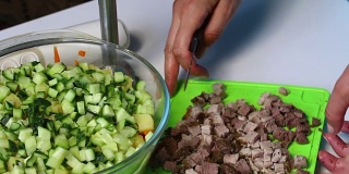 俄罗斯肉沙拉配蔬菜和蛋黄酱。一位妇女切下烤肉准备做沙拉。