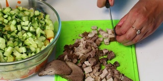 俄罗斯肉沙拉配蔬菜和蛋黄酱。一位妇女切下烤肉准备做沙拉。