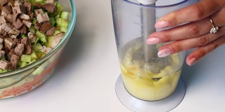 俄罗斯肉沙拉配蔬菜和蛋黄酱。一位妇女正在用搅拌机搅拌蛋黄酱做沙拉。