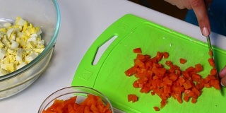 俄罗斯肉沙拉配蔬菜和蛋黄酱。一位妇女在砧板上切煮熟的胡萝卜。
