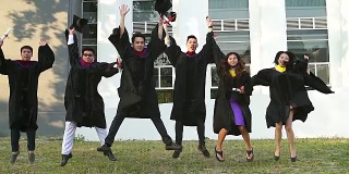 成功的毕业生穿着学位服，拿着学位证书，看着相机，微笑着跳到户外拍照。