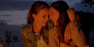 两个年轻的白人女孩晚上坐在大自然的火炉旁，笑着，微笑着