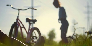 一个骑自行车的年轻人正在弯曲双腿，后面的女孩正在喝水