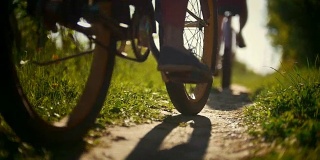 在一个阳光明媚的日子里，骑自行车的人的腿，两个年轻的女孩在绿色的森林小径上经过