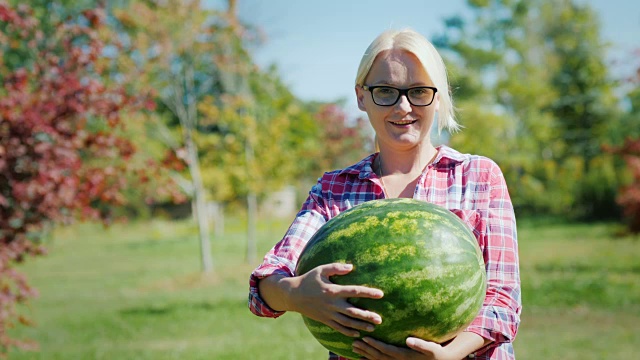 一个女农民拿着一个大西瓜，看着镜头，微笑着