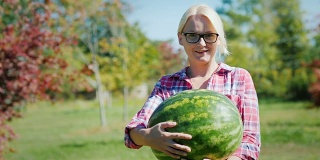 一个女农民拿着一个大西瓜，看着镜头，微笑着