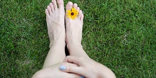 女人的脚踩在草地上，草地上开着黄花。高清视频运动