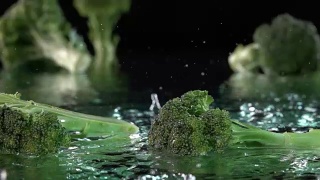 绿色的西兰花落在水面与水在黑色的飞溅气泡视频素材模板下载