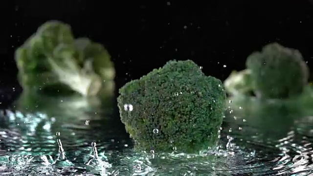 绿色的西兰花落在水面与水在黑色的飞溅气泡