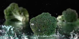 绿色的西兰花落在水面与水在黑色的飞溅气泡