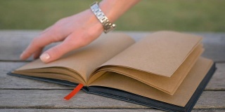 风在长凳上翻动一本空白的书。非常漂亮的设计师笔记本在街上。女人的手合上拿起了书