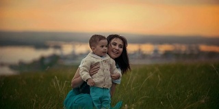 一个女孩正坐在绿色的草地上，她的旁边是她的宝宝，他们在笑着，夕阳西下的夏日