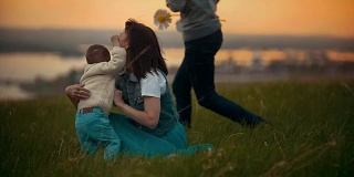 年轻的妈妈和她的孩子在草地上玩耍，孩子是快乐的，夏天的傍晚，夕阳