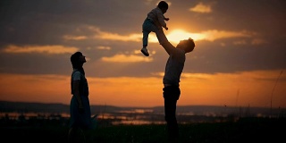 一家人站在夕阳的背景下，父亲将儿子抛向空中，这是一个夏日的傍晚