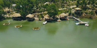 木平房与茅草屋顶和船码头上的湖在度假酒店无人机的观点。滨水别墅、山、湖、水、野别墅、空中景观