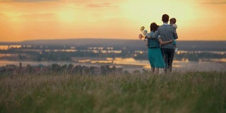 一家人三人在大自然中休息，爸爸妈妈和儿子去拥抱，橙色的夕阳