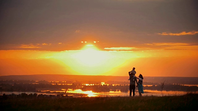 一家人在夏日的夕阳下散步，爸爸妈妈手牵着手，儿子坐在他的肩膀上