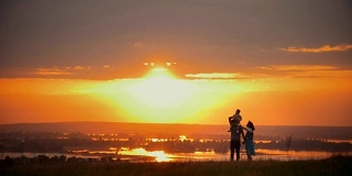 一家人在夏日的夕阳下散步，爸爸妈妈手牵着手，儿子坐在他的肩膀上