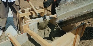 在建筑工地使用混凝土。工人们把混凝土放进一个木模里。建筑工地繁重的体力劳动