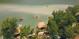 热带平房与茅草屋顶和船码头岸上绿色的湖在度假酒店山鸟瞰图。别墅在岸边的山中湖在异国情调的自然在水上别墅度假无人机的观点