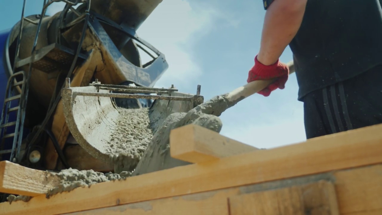 工人从工业搅拌机中取出混凝土，就像铲子一样工作。建筑工地繁重的体力劳动。低角度拍摄