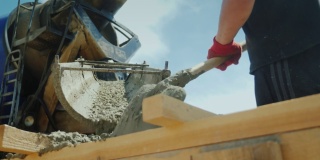 工人从工业搅拌机中取出混凝土，就像铲子一样工作。建筑工地繁重的体力劳动。低角度拍摄