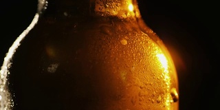 黑色背景上的一瓶冰啤酒。一束光美丽地照亮了它，它慢慢地旋转