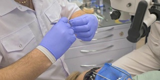 医生使用显微镜。牙医在现代牙科诊所里治疗病人。牙齿矫正师与助手一起工作。作业采用围堰进行。医生和助手戴着防护口罩工作。