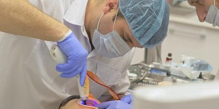 牙医在一间现代化的牙科诊所里为病人治疗。牙齿矫正医师有一个助手。病人用蓝色激光牙消毒。橙色的玻璃百叶窗用于保护眼睛。