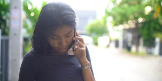 年轻的亚洲女孩讲电话在联排别墅村庄