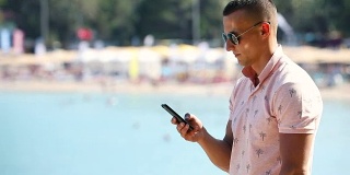 年轻人在海边使用智能手机。一个在海边玩手机应用的家伙。