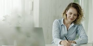 年轻女子用笔记本电脑工作，在办公室喝咖啡