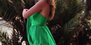 美丽的女人在热带棕榈树附近摆姿势的绿色裙子