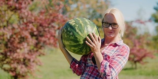 秋高气爽，收获多多。一个农妇正拿着一个又大又重的西瓜