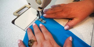 中年妇女在缝纫机上手工缝制蓝色织物