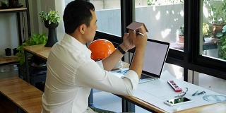 建筑师坐在电脑前，拿着房子的小模型。