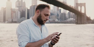 严肃的欧洲商人在令人惊叹的纽约日落美景的4K智能手机messenger应用程序上输入信息
