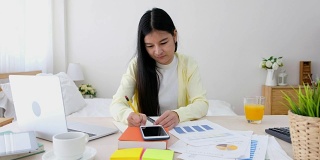 亚洲女性自由职业者打字工作与笔记本电脑在桌子上在家里的卧室。在家工作的概念。在家工作概念