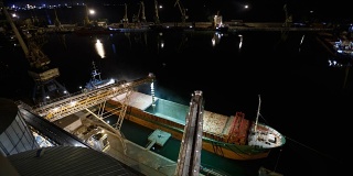 在海港的筒仓码头，从上方通过主干将粮食作物装载到打开货舱的散货船上的夜间时间间隔。谷物主要转运。运输农产品