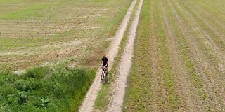 空中慢镜头:一名男子骑着自行车沿着乡间小路穿过耕地