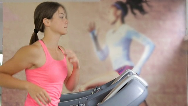 在健身房跑步机上跑步的漂亮的年轻女子。