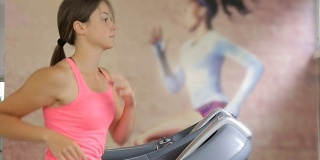 在健身房跑步机上跑步的漂亮的年轻女子。