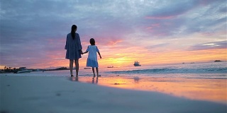 小女孩和爸爸的剪影在日落的海滩上