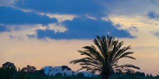 日落在白色的房子和棕榈树。夕阳下棕榈树的剪影。时间流逝。间隔拍摄。