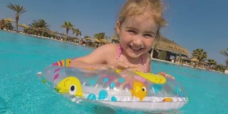 在炎热的夏日里，快乐的小女孩在室外游泳池里玩五彩缤纷的充气圈。孩子们在热带度假胜地玩耍。孩子们学游泳。家庭海滩度假。